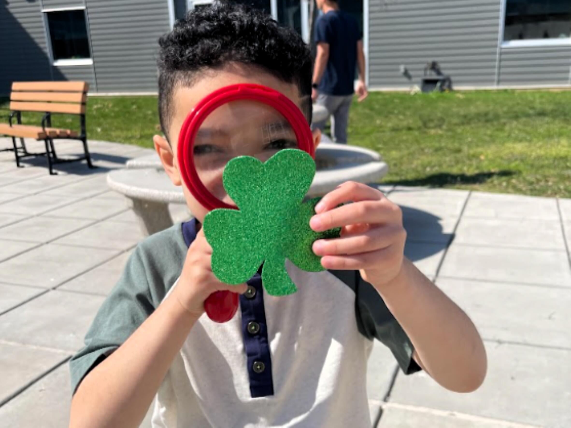 Enf- student looking through magnifying glass at a glitter shamrock
